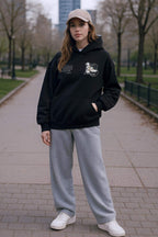 Woman wearing black oversized R3 The Messiah John 3:16 premium cotton hoodie with gray sweatpants and beige cap outdoors