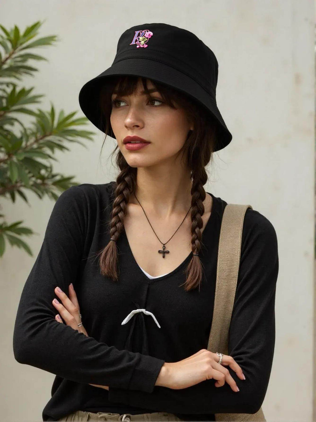 Black bucket hat with pink embroidered rose logo worn by woman with braided hair