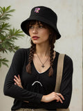 Black bucket hat with pink embroidered rose logo worn by woman with braided hair