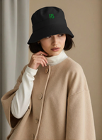 R3 Bucket Hat Noir Edition black bucket hat with green logo on woman wearing beige coat and white turtleneck
