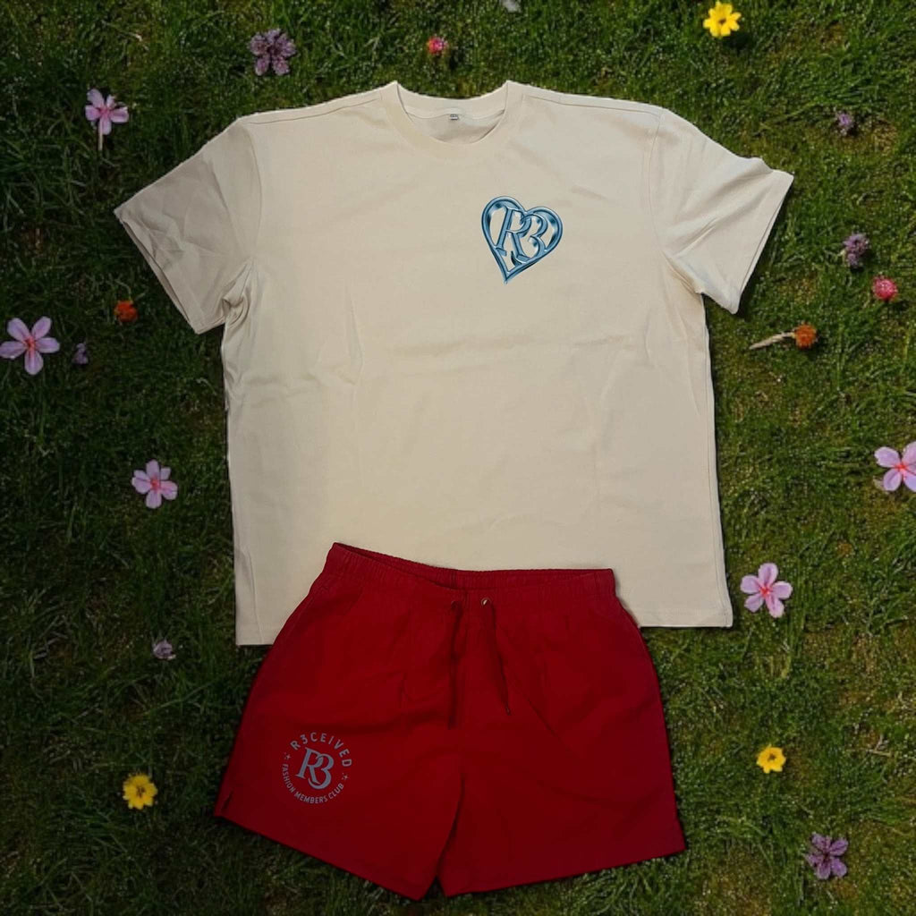 Men's red R3 Fashion Members Club swimming trunks with pockets and elastic waistband, paired with a cream t-shirt, displayed on grass with flowers.