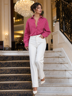 Vrouwelijk model draagt de rode gestreepte blouse met witte relaxed jeans op een marmeren trap