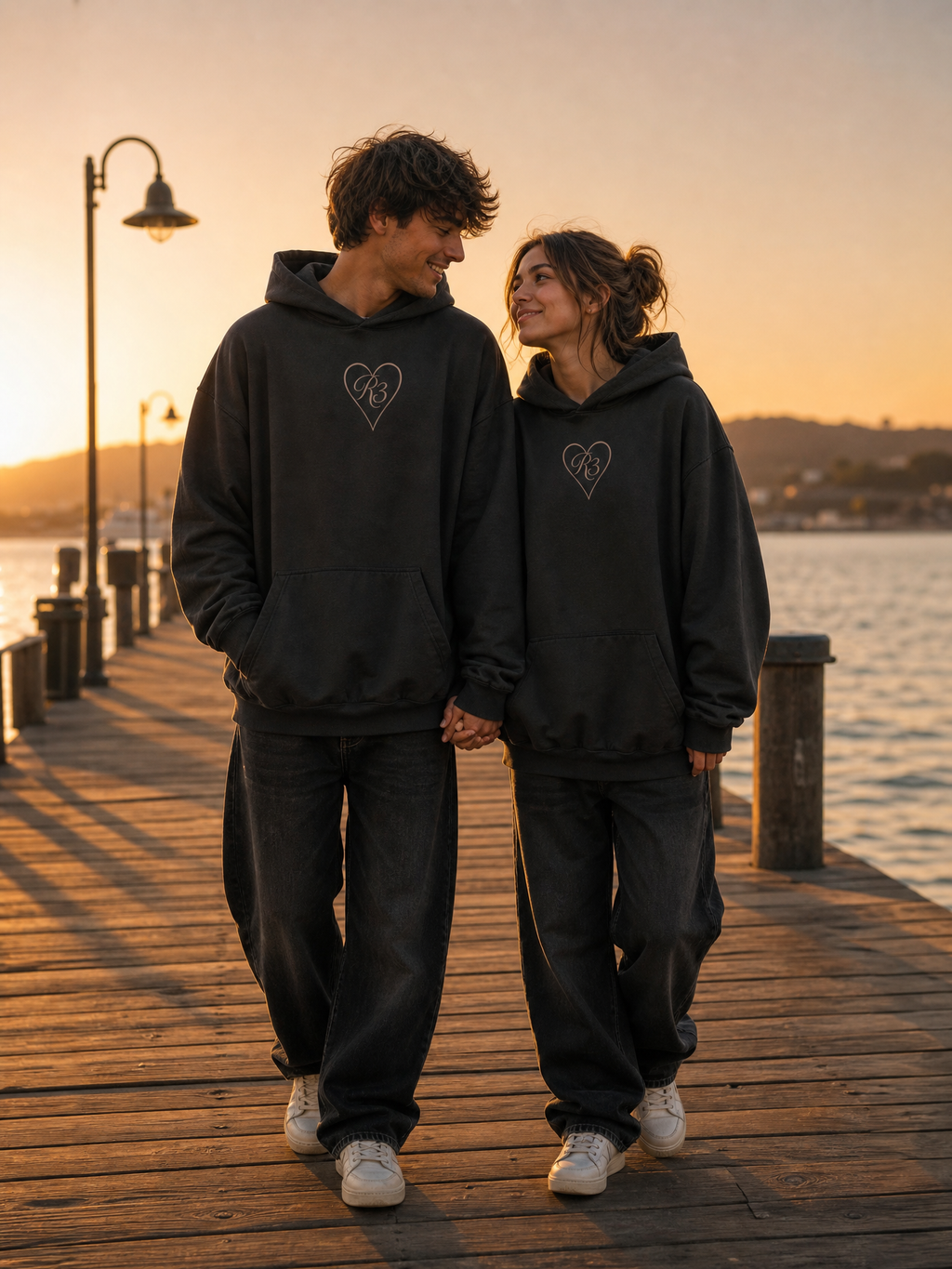 R3CEIVED True Love hoodie - koppel voorkant, mannelijk en vrouwelijk model bij zonsondergang op een pier