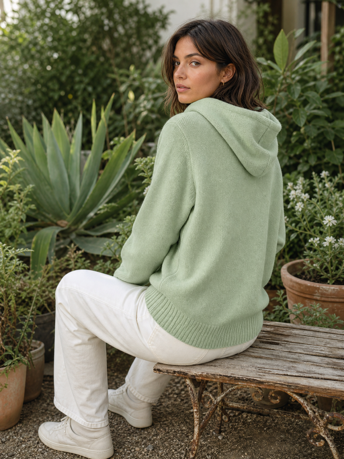 Gebreide hoodie lichtgroen - model zit op tuinbankje