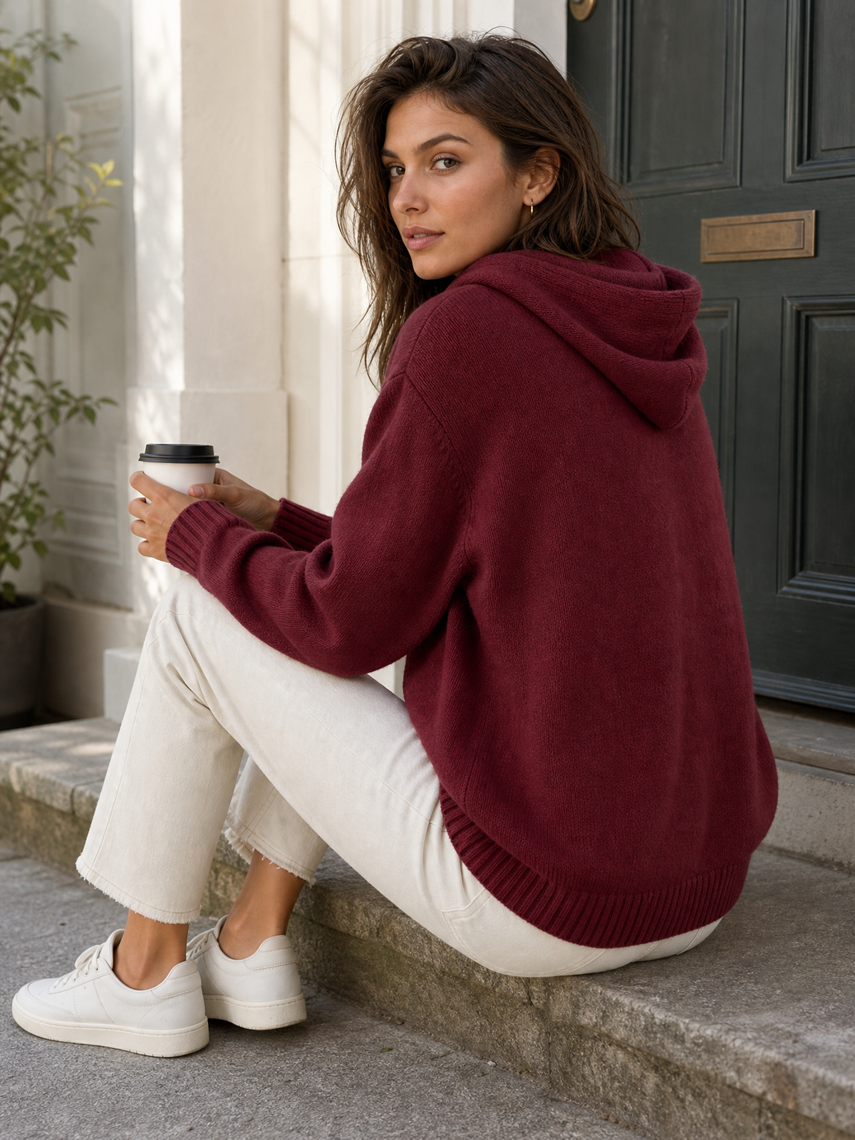 Gebreide hoodie bordeauxrood - model zit op stoep met koffie