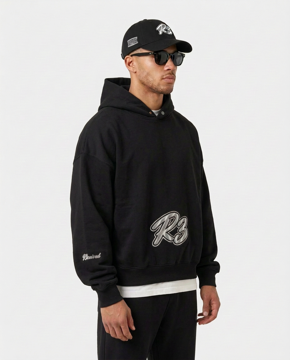 Model wearing the black Hustler Mid R3 hoodie by R3CEIVED, three-quarter view