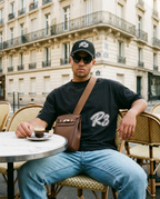Man in R3CEIVED Hustlers T-shirt wearing the Sinclair crossbody bag in Brown at a Paris café